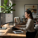 Professional woman working productively at home office desk wearing wireless smart earbuds with natural lighting